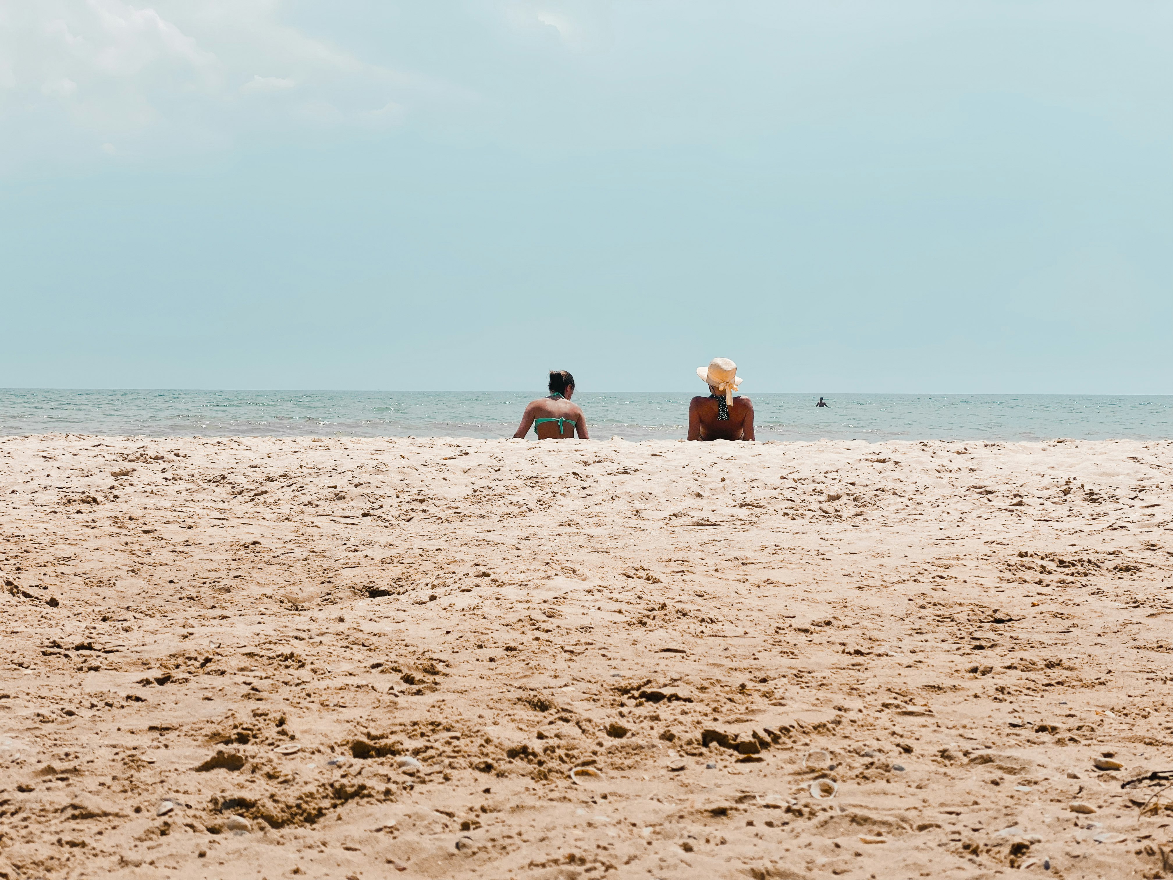 2 women sitting on beach sand during daytime